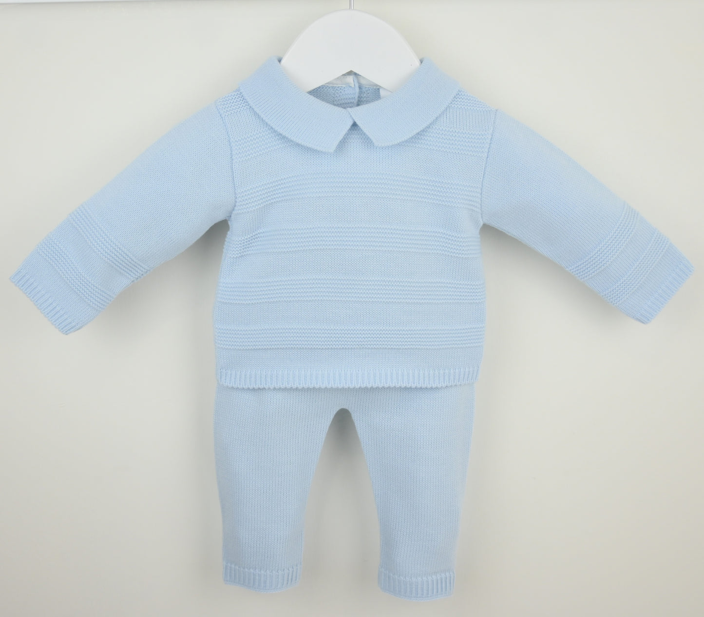 A light blue ribbed knit two-piece outfit for a doll or baby, featuring a long-sleeve collared top and matching pants, displayed on a white hanger against a light beige background.