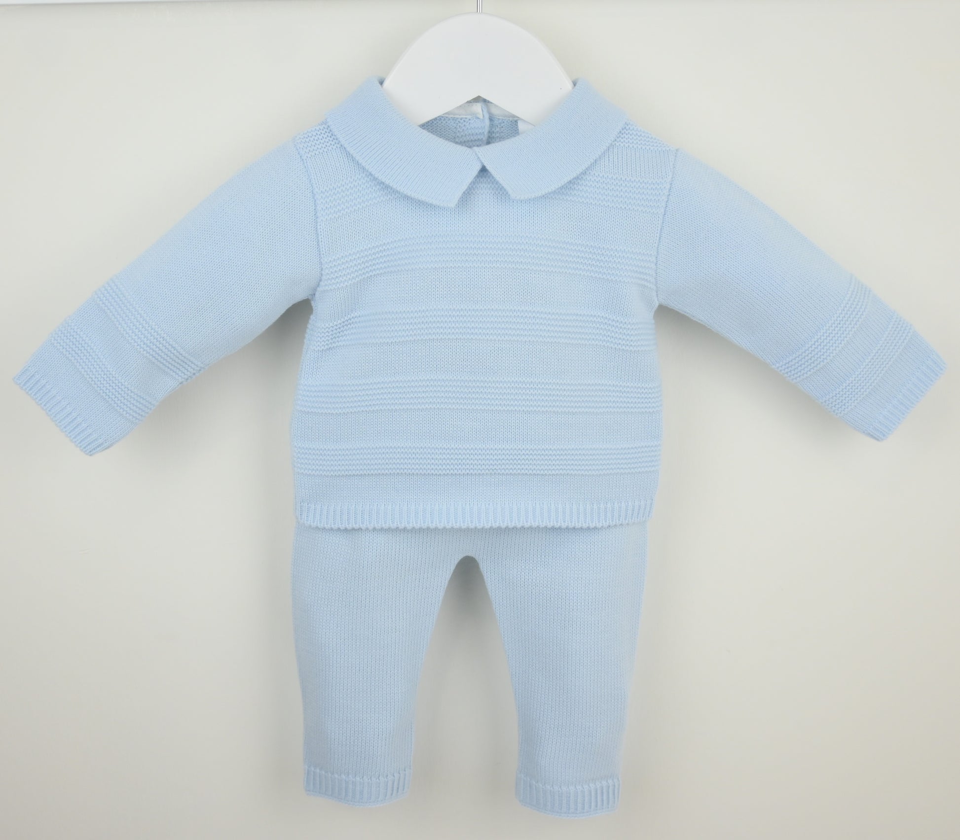 A light blue ribbed knit two-piece outfit for a doll or baby, featuring a long-sleeve collared top and matching pants, displayed on a white hanger against a light beige background.