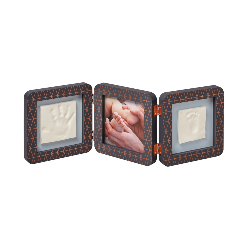 A three-panel fold-out keepsake photo frame with textured dark brown and orange patterned borders. The left and right panels contain white handprint and footprint cavities, and the center panel holds a printed photo of a baby's face and feet.